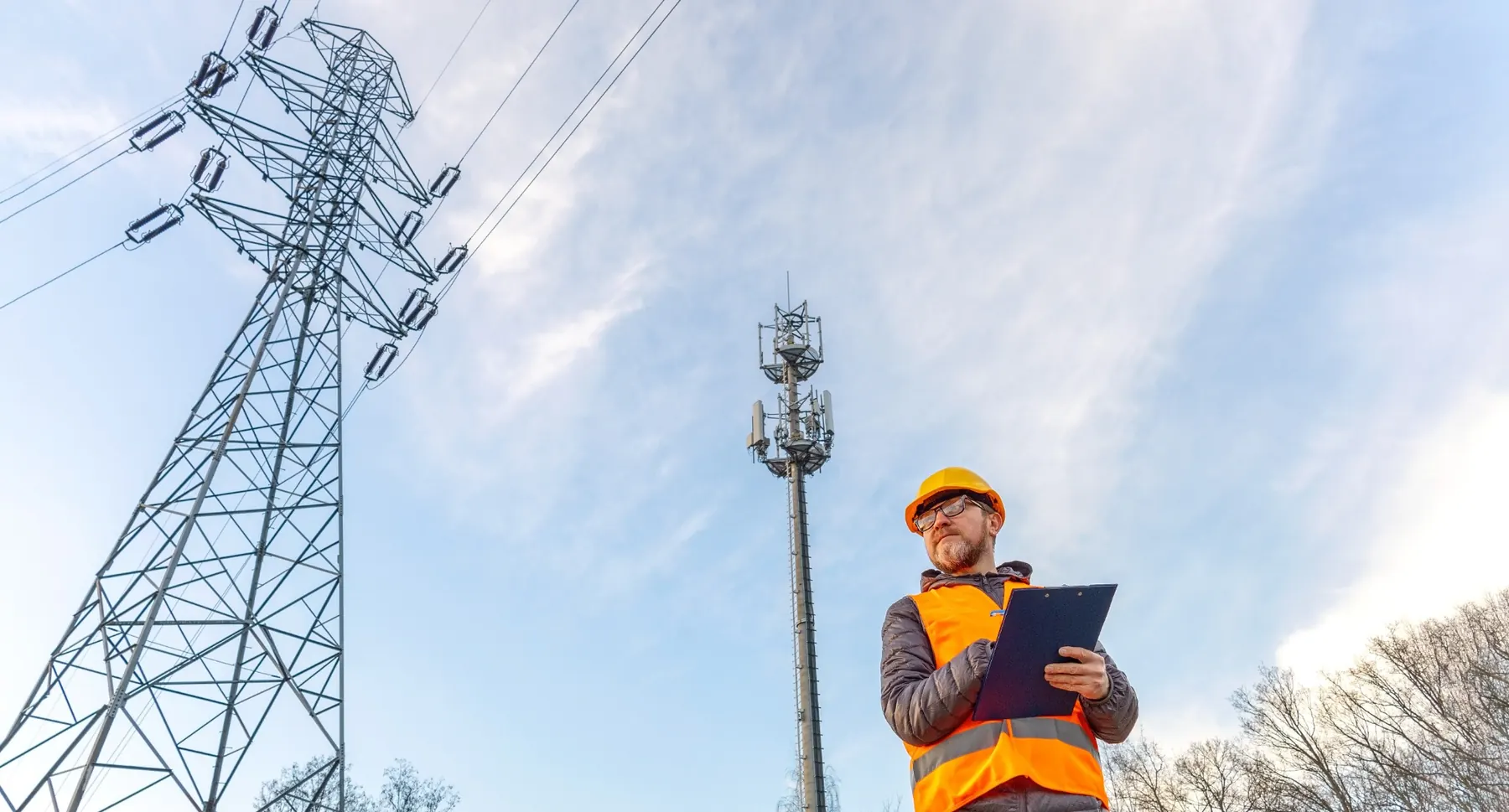 Electrical engineer inspecting power infrastructure near transmission and communications equipment